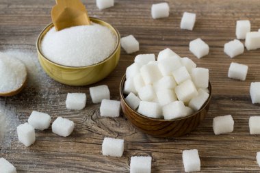 Bambu kasesinde beyaz şeker küpleri, tahtadan yüzeyde granüle şeker.