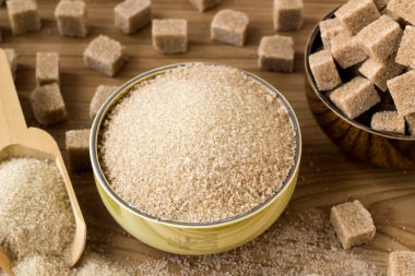 Doğal, kahverengi granüllü şeker bambu kasesinde kahverengi şeker küpleri ve tahta yüzeyde tahta kürek.