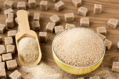 Doğal, kahverengi granüllü şeker bambu kasesinde kahverengi şeker küpleri ve tahta yüzeyde tahta kürek.