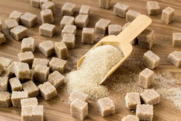 Tahta kürekte doğal, kahverengi granüllü şeker ve tahtadan yüzey üzerinde kahverengi şeker küpleri.
