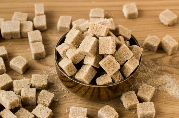 Tahta yüzeyde bambu kasesinde doğal, kahverengi şeker küpleri, yakın plan çekilmiş.