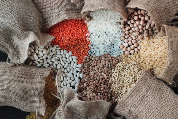 Red lentils,chickpeas,white rice and bulgur pouring from jute sack onto black surface with copy space.Harvest concept