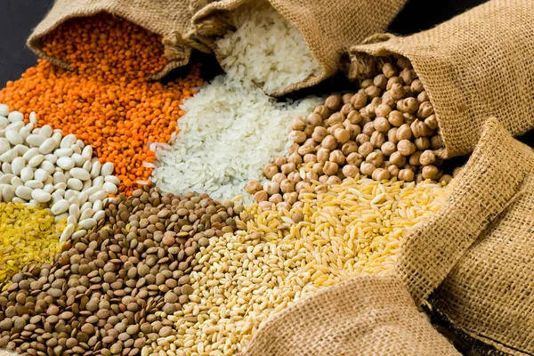 Red lentils, chickpeas, white rice and bulgur pouring from jute sack onto black surface with copy space.Harvest concept