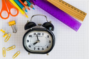 Siyah renkli klasik çalar saat ve renkli okul malzemeleri kareli kağıtta.
