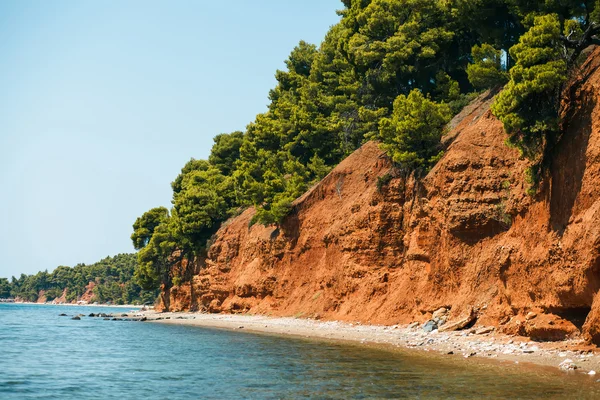 Beach with red land and green pines in Metamorfosi, Greece — Stock Photo, Image