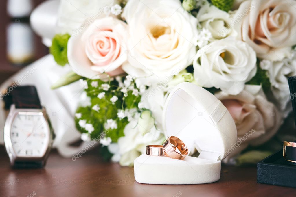 Gold wedding rings in white gift box in shape of heart and wedding bouquet.