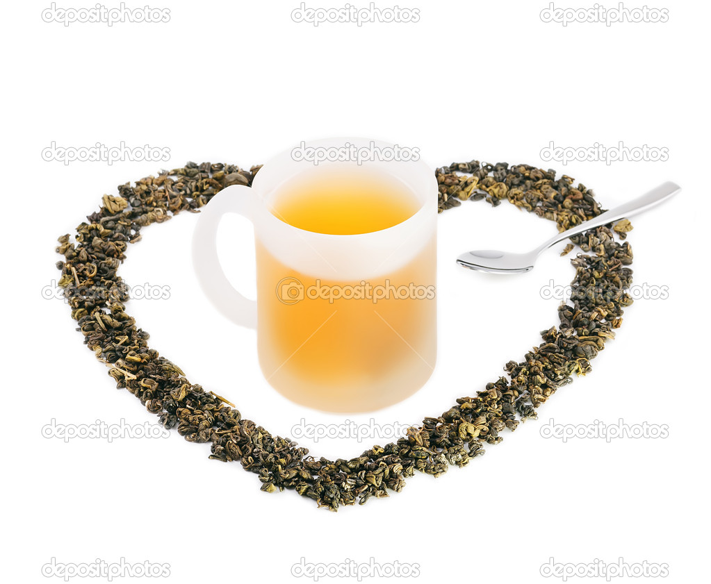 Cup of green tea placed in tea leaves in shape of heart.