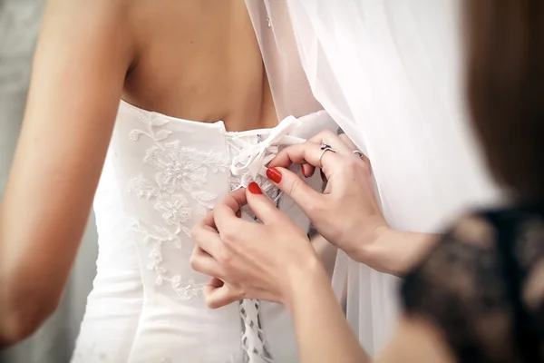 Brudtärna hjälper bruden att sätta på ett bröllopsklänning. — Stockfoto