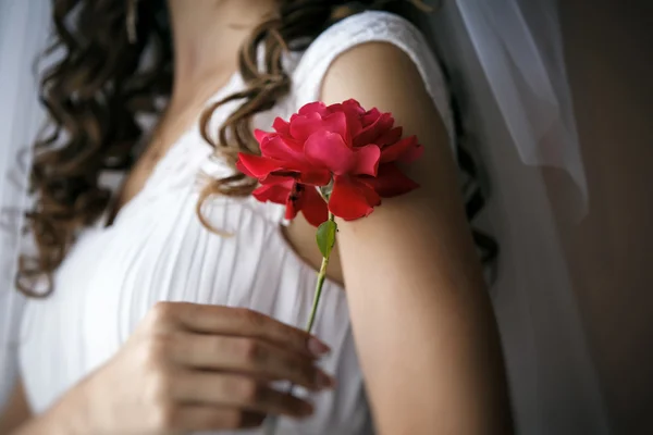 Bride gently touches her shoulder by rose. — Stock Photo, Image