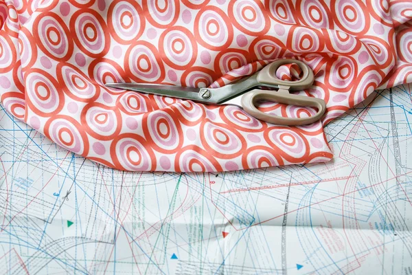 Scissors and silk material with pattern in background. Focused o — Stock Photo, Image