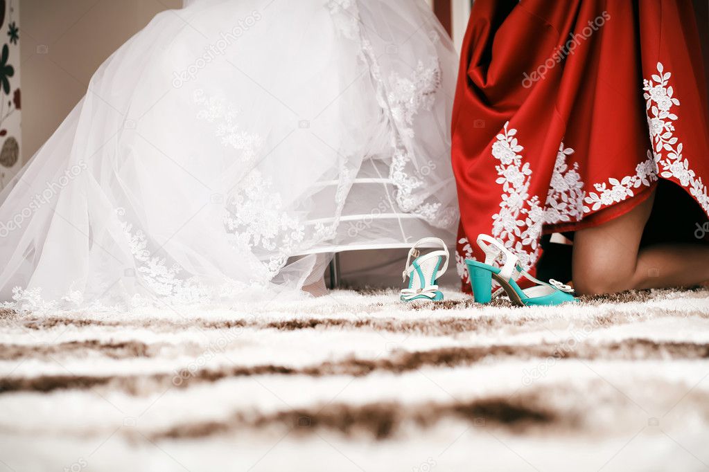 Bridesmaid helps to bride to put on cyan wedding shoes.