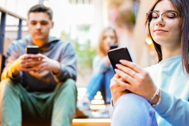 Bir grup arkadaş cep telefonu kullanıyor merdivenlerde oturan ve akıllı telefonlara yazı yazan öğrenciler.