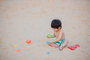 Kumsalda plaj oyuncaklarıyla oynayan tatlı bir oğlan..