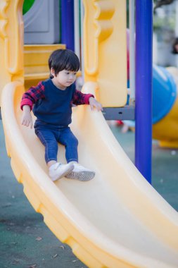 Küçük çocuk parkta slaytta oynuyor..