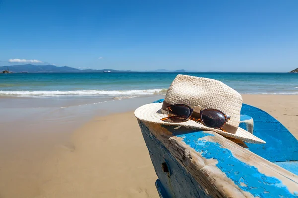 Hut und Sonnenbrille auf Boot am Strand — Stockfoto