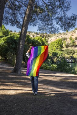 Göl kenarında elinde Gay Gökkuşağı Bayrağı tutan orta yaşlı bir lezbiyen kadın. Özgürlük kavramı