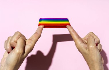 Pembe arka planda LGBT bileziği olan kadın elleri
