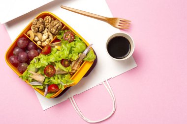 Healthy Food in Plastic container ready to eat with homemade lettuce salad with tomato, onion, corn, tuna, roga grapes, walnuts and cashews in paper bag fro, above. Take away concept