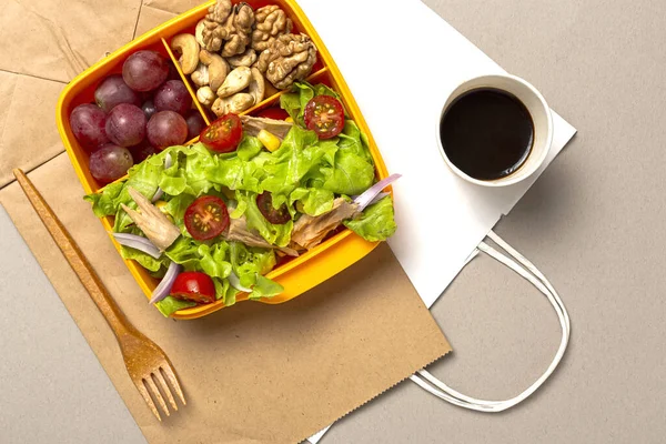 Healthy Food in Plastic container ready to eat with homemade lettuce salad with tomato, onion, corn, tuna, roga grapes, walnuts and cashews in paper bag fro, above. Take away concept