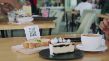 Kadın, kafeteryada nakit olmadan dijital ödeme yapmak için akıllı telefon kullanarak QR kodunu tarıyor. Menüyü ve siparişi seçin ve indirimi toplayın. Cüzdan, teknoloji, online ödeme, kredi kartı, banka uygulaması, tarama