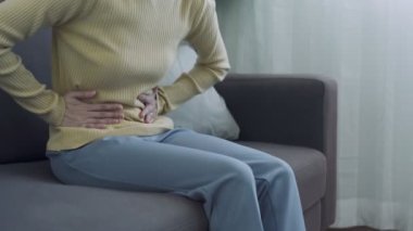 Regl ve regl sancıları çeken Asyalı kadınlar. Kanepede acı içinde oturan bir kız. Kadında mide iltihabından kaynaklanan şiddetli karın ağrısı vardı. konsept mide ağrısı.