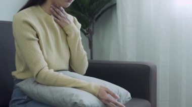 Kadın boğazı ağrıdığı için elini boynuna koydu. Bademcik iltihabı boğaz ağrısına neden olur. Boğaz ağrıları pek çok nedenden kaynaklanabilir ve sıcak su alıp antibiyotik alarak tedavi edilebilir..