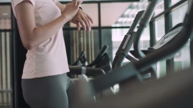 Genç sporcular egzersiz kaydetmek ve kalorileri yakmak için akıllı saate basıyorlar. Bir kadın uyluk egzersizi için eliptik makine üzerinde egzersiz yapıyor. Fitness konsepti.