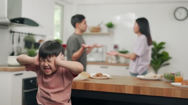 亚洲男孩坐在那里 用手紧闭着耳朵 因为父母在家里吵架 家庭问题使儿童今后有心理问题 家庭中的家庭问题 — 图库视频影像