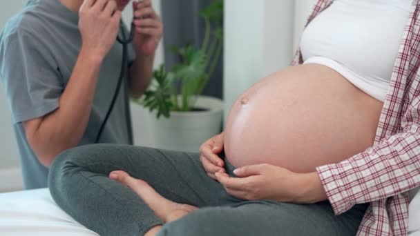 妊娠中の女性と夫をコンセプト 夫は赤ちゃんの声の心を聞くために聴診器を使用しています 胎児の音に耳を傾け異常の可能性を発見 — ストック動画