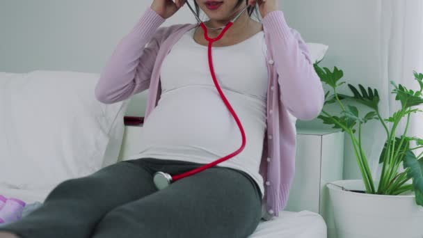 妊婦は聴診器を使って赤ちゃんの声を聞きます 妊娠中の女性が赤ん坊の心拍をチェックしている 妊婦の幸福の概念 — ストック動画
