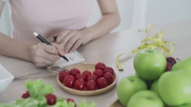 Sağlıklı beslenme konsepti. Kadın diyeti yüzünden yemeklerde kalori kontrolü için diyet planı yazıyor. Kadın kilo vermek için domatesi seçti.