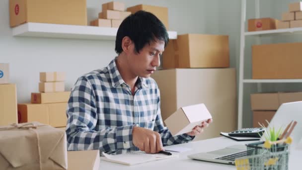 アジアの男性ビジネスオーナーは宅配会社経由で配達のためのオンライン注文を準備しています 中小企業の所有者は ノートをチェックし 倉庫の詳細を収集し 配達のためにそれらを収集しています — ストック動画