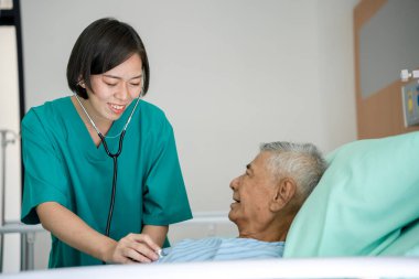 Asyalı kadın doktor kalp rahatsızlığı olan yaşlı bir adamın kalp ciğerlerini incelemek için stepthoscope kullanıyor. Profesyonel doktorlar, hastanedeki hastalar için zihinsel terapi ve danışmanlık hizmeti verirler..