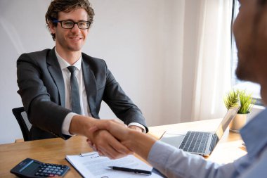 Genç Avrupalı işadamı, bir müşteri bir evi imzalamayı kabul ettikten sonra başarıyla gülümsüyor. Sigortayla tam kontratlı el sıkışma. İpotek, kira, satın alma, satma, taşınma konsepti.
