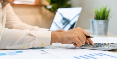 Bir adam istatistiksel grafiklerden şirket kârını hesaplamak için hesap makinesi kullanır. Haritalara, hesap tablolarına, banka hesaplarına, istatistiklere, ekonomiye, veri analizine, borsaya bakan işadamları