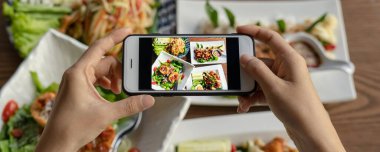 Tayland yemeği. El, restorandaki yemek masasında yemek fotoğrafı çekmek için bir cep telefonu kullanıyor. Cep telefonu kavramlı fotoğrafçılık