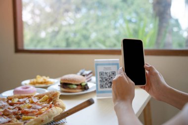 Kadınların elleri yemek menüsünü seçmek için QR kodunu tarıyor. İndirim için tarama yap ya da yiyecek için ödeme yap. Para transferi için telefon kullanma ya da nakit olmadan internet üzerinden para ödeme kavramı..