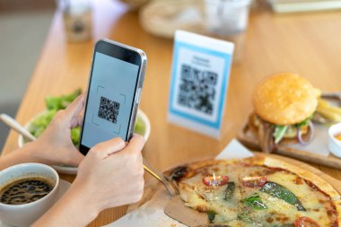 Kadının eli, restoranda bir QR kodunu taramak için telefon kullanıyor. İndirim almak ya da yemek için ödeme yapmak için. Para aktarmak için telefon kullan ya da internetten nakit ödeme yap..