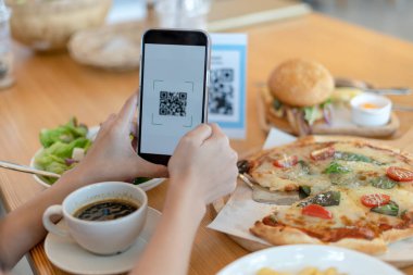 Kadınların elleri yemek menüsünü seçmek için QR kodunu tarıyor. İndirim için tarama yap ya da yiyecek için ödeme yap. Para transferi için telefon kullanma ya da nakit olmadan internet üzerinden para ödeme kavramı.