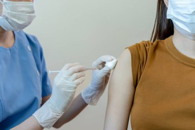 Tıbbi maske takan Asyalı kadın bir doktordan koronavirüs aşısı alıyor. İnsanlar COVID-19 'a karşı aşılanmış virüsün bulaşmasını önlemek ve yayılmasını engellemek için..