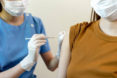 Tıbbi maske takan Asyalı kadın bir doktordan koronavirüs aşısı alıyor. İnsanlar COVID-19 'a karşı aşılanmış virüsün bulaşmasını önlemek ve yayılmasını engellemek için..