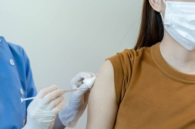 Tıbbi maske takan Asyalı kadın bir doktordan koronavirüs aşısı alıyor. İnsanlar COVID-19 'a karşı aşılanmış virüsün bulaşmasını önlemek ve yayılmasını engellemek için..