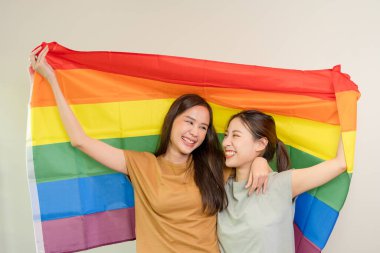 LGBT grubu. Güzel görünümlü lezbiyen çiftler gökkuşağı bayraklarını parlak bir şekilde örterler. Asyalı çift birbirine mutlu bir şekilde sarılıyor, aşık.