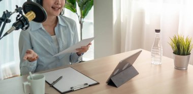 Parlak Asyalı kadınlar mikrofon ve bilgisayar kamerasıyla podcast kaydediyor. Ev stüdyosunda çalışan genç bir kadın. yayın stüdyosu konsepti