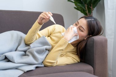 Ateşli, burnu akan ve COVID-19 salgını sırasında öksüren Asyalı bir kadın..