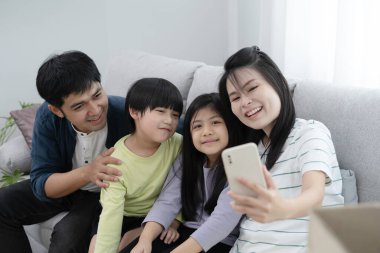 Aile babası, küçük kızı ve oğlu yeni evdeki oturma odasındaki kanepede rahatlar ve akıllı telefonla gülümseyerek ve neşeli bir kahkahayla selfie çekerler..