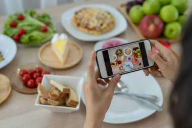 Restoran masasında yemek fotoğrafı çekmek için cep telefonu kullanan bir eleştirmen. İnternette paylaşmak için restoranın eleştirisini yazmak için fotoğraf çekin..