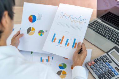 Bir adam istatistiksel grafiklerden şirket kârını hesaplamak için hesap makinesi kullanır. Haritalara, hesap tablolarına, banka hesaplarına, istatistiklere, ekonomiye, veri analizine, borsaya bakan işadamları