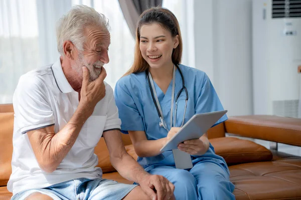 助理医生使用平板电脑向老年男子解释治疗和检查后的检查结果 护理人员笑着鼓励和关心病人 健康保险 疗养院 — 图库照片