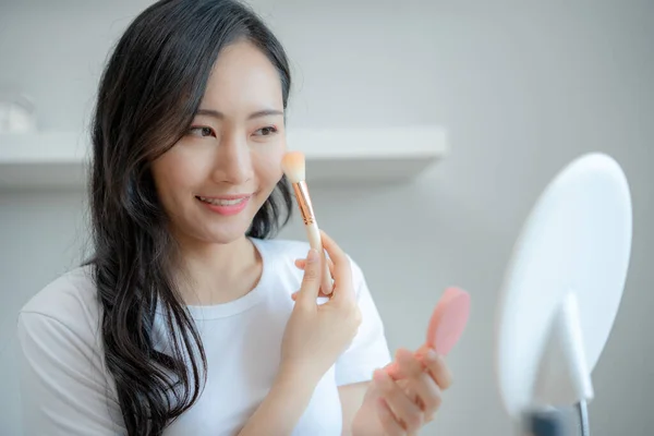 Beautiful Asian woman sitting in front of a mirror with makeup. face of a healthy woman applying cream,makeup, use brush on cheek
